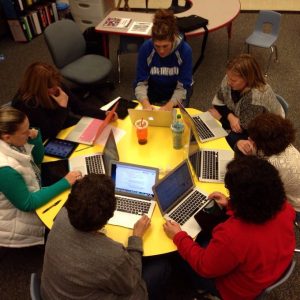 Seven teachers with laptops around a circular table